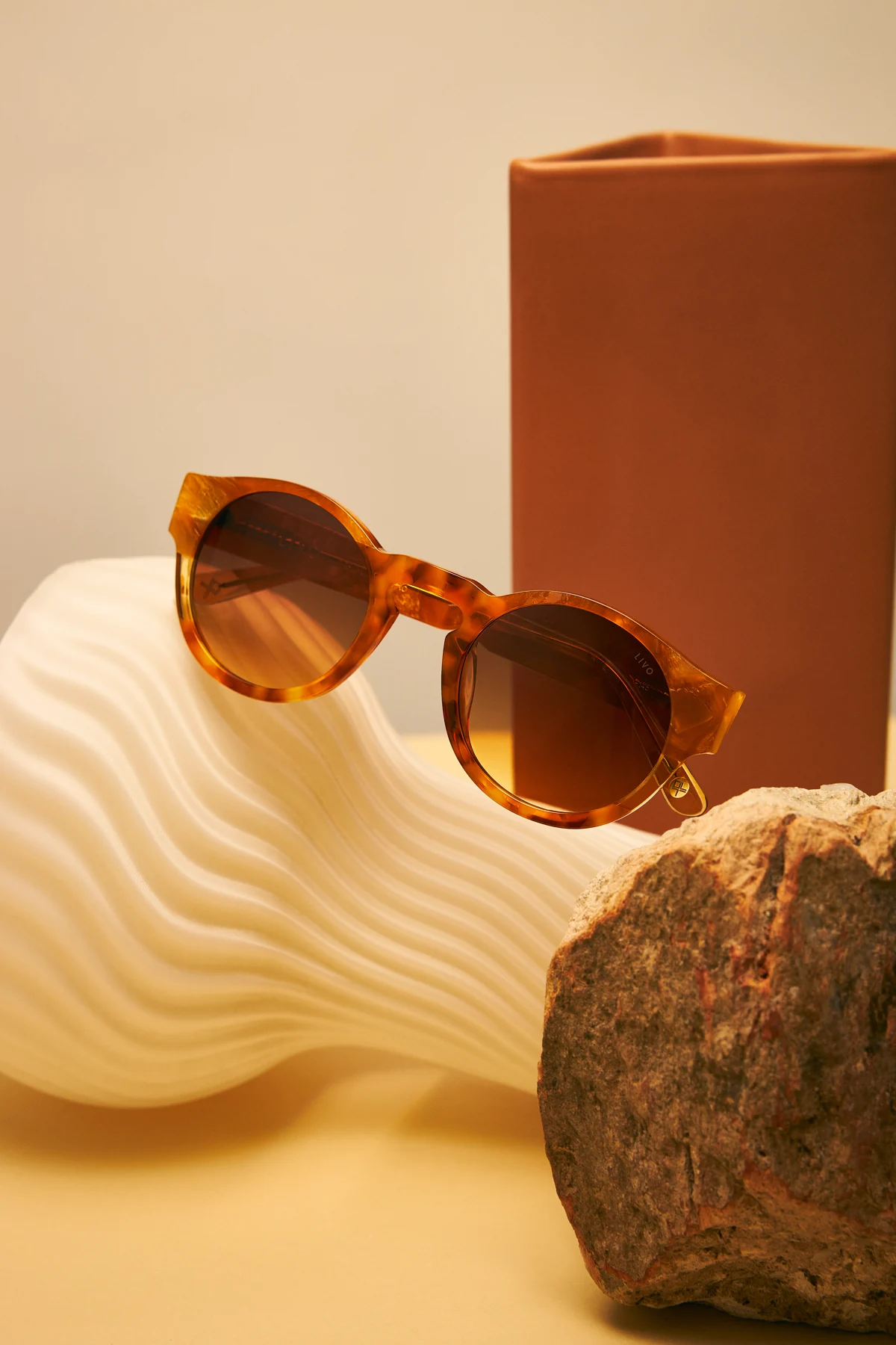 Amber JULES sunglasses with gradient lenses, photographed beside sand-coloured sculpture and stone