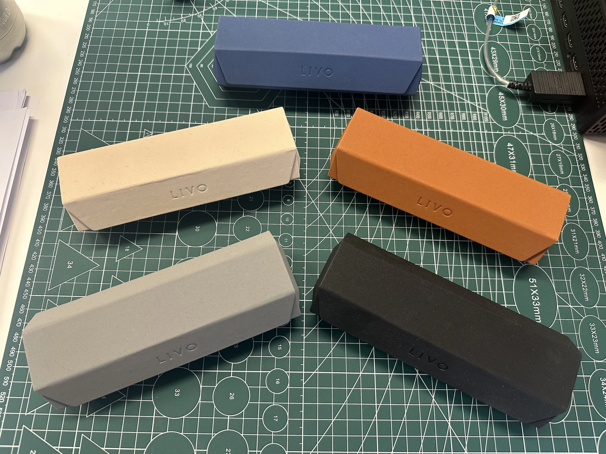 Five LIVO Exagonale cases in blue, cream, orange, pale grey and black arranged on a green cutting mat