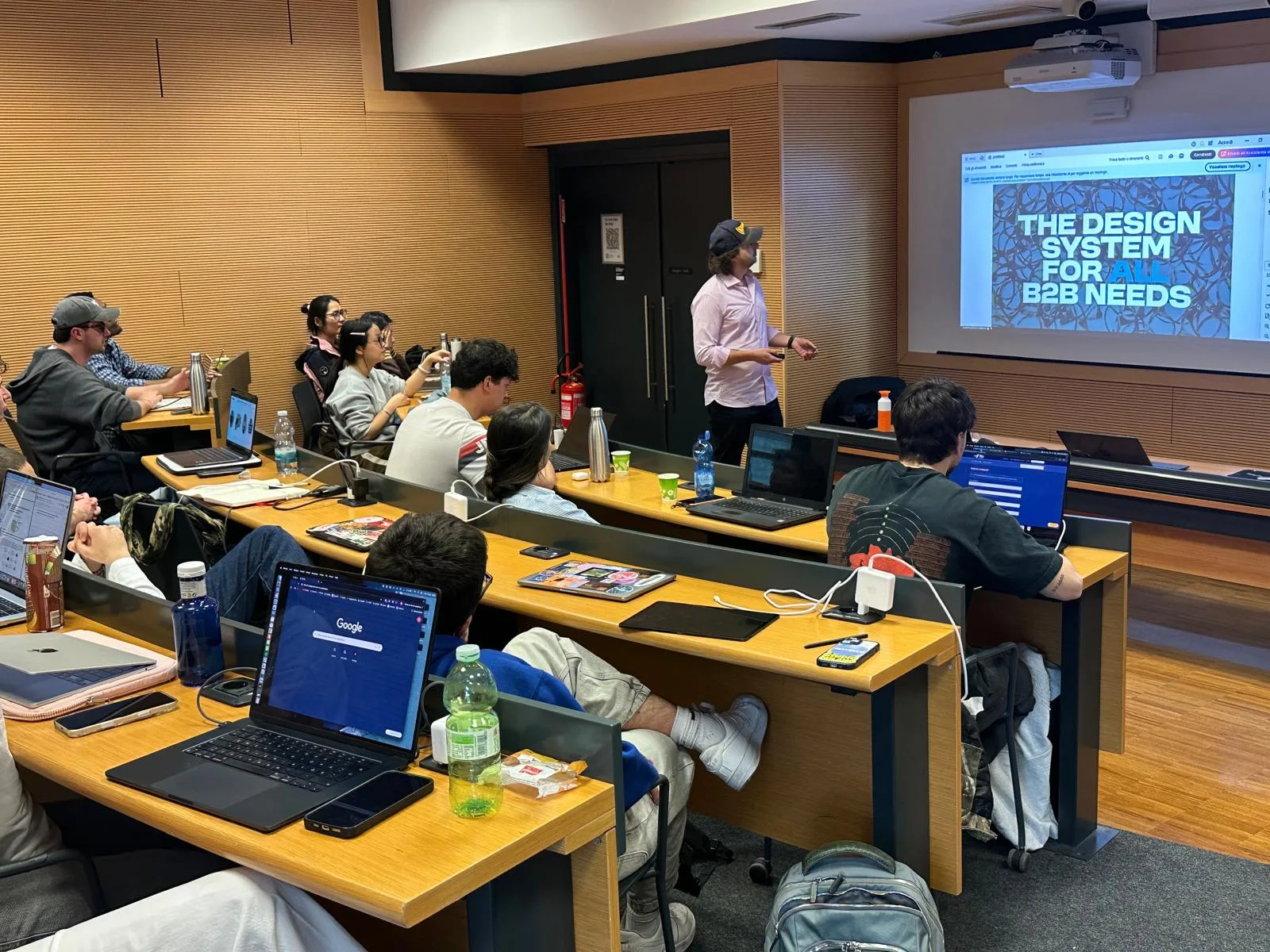 Lucas Milossi speaking beside a MILOSSI presentation while students follow the session
